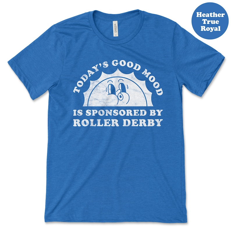 Op de afbeelding: Een blauw T-shirt met een witte afbeelding waarop staat "Today's Good Mood Is Sponsored By Roller Derby". De afbeelding toont een cartoonzon met een glimlachend gezicht.