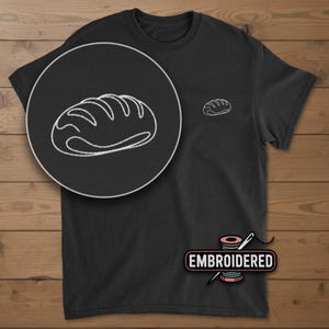 May include: Black t-shirt with a white embroidered bread loaf design on the chest and a larger, detailed version in a circular inset. The word "EMBROIDERED" is displayed below the shirt. The shirt is made of a soft material.