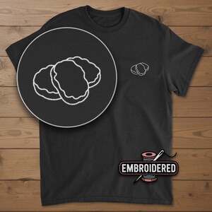 May include: Black t-shirt with a white embroidered design of three chicken nuggets. A larger, detailed view of the nugget design is in a circular inset. The word "EMBROIDERED" is displayed below the shirt.