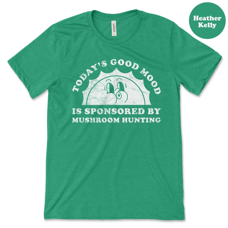 May include: Green t-shirt with a white graphic that says "Today's Good Mood Is Sponsored By Mushroom Hunting". The graphic features a cartoon sun with a smiling face.