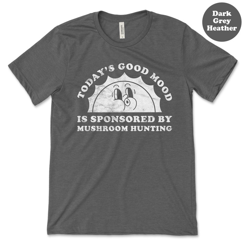 May include: Dark heather grey t-shirt with a white graphic of a smiling sun with the text "Today's Good Mood Is Sponsored By Mushroom Hunting".