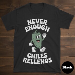 Peut inclure: T-shirt noir avec l'inscription blanche "NEVER ENOUGH CHILES RELLENOS". Un personnage de piment vert de dessin animé fait signe. Le t-shirt est de style col rond.