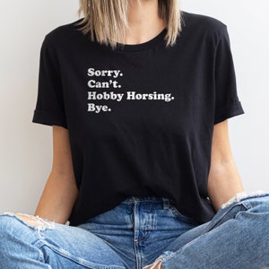 May include: A black t-shirt with white text that reads "Sorry. Can't. Hobby Horsing. Bye."