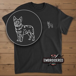May include: Black t-shirt with a white embroidered dog design. The shirt features a large circular detail of the dog and a smaller version on the chest. The word "EMBROIDERED" is printed on a pink spool of thread.
