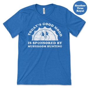 May include: A blue t-shirt with a white graphic of a smiling sun with the text "Today's Good Mood Is Sponsored By Mushroom Hunting".