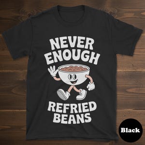 May include: Black t-shirt with the text "NEVER ENOUGH REFRIED BEANS". The design features a cartoon bowl of refried beans with arms and legs. The bowl is white with a brown filling, and the text is in white.