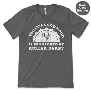 Op de afbeelding: Donkergrijs heather t-shirt met een witte afbeelding van een lachende zon met de tekst "Today's Good Mood Is Sponsored By Roller Derby".
