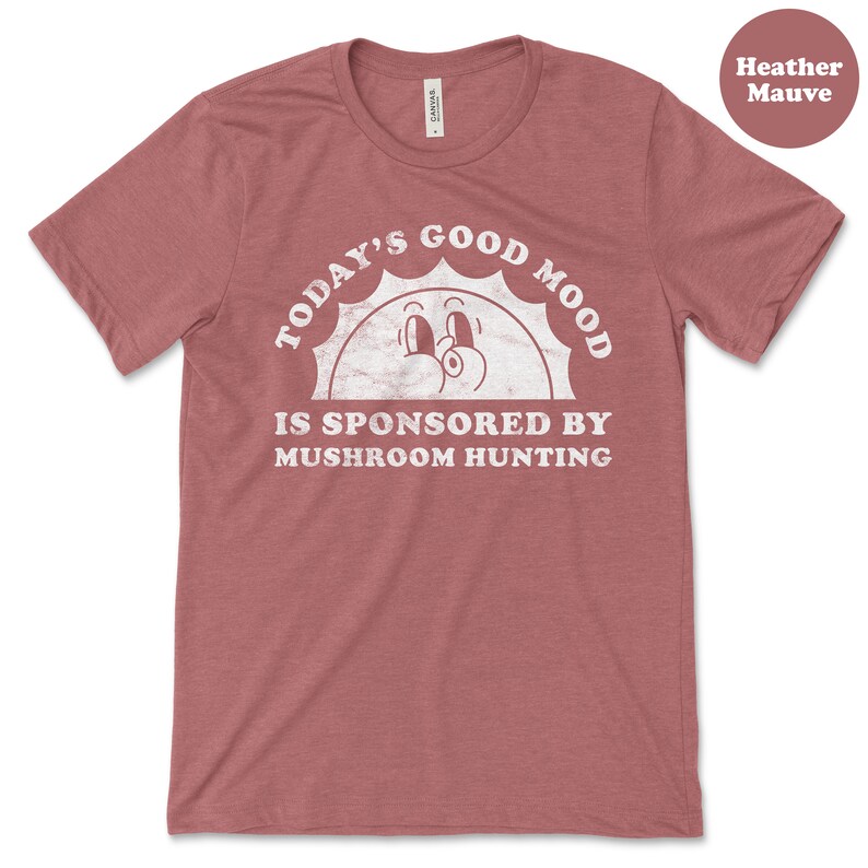 May include: Heather mauve t-shirt with a white graphic of a smiling sun with the text "Today's Good Mood Is Sponsored By Mushroom Hunting."