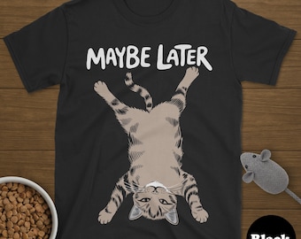 May include: Black t-shirt with the text "MAYBE LATER" above a cartoon cat hanging upside down. The cat is tan and brown with stripes. A bowl of cat food and a gray toy mouse are also visible.