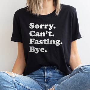 May include: A black t-shirt with white text that reads "Sorry. Can't. Fasting. Bye."