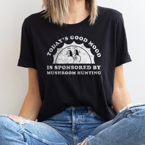 May include: Black t-shirt with a white graphic of a smiling sun with the text "Today's Good Mood Is Sponsored By Mushroom Hunting."