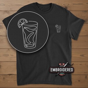 May include: Black t-shirt with a white embroidered design of a cocktail with a lemon slice. The design is on the left chest and a larger version is in a circle on the front. The word "EMBROIDERED" is below the design.