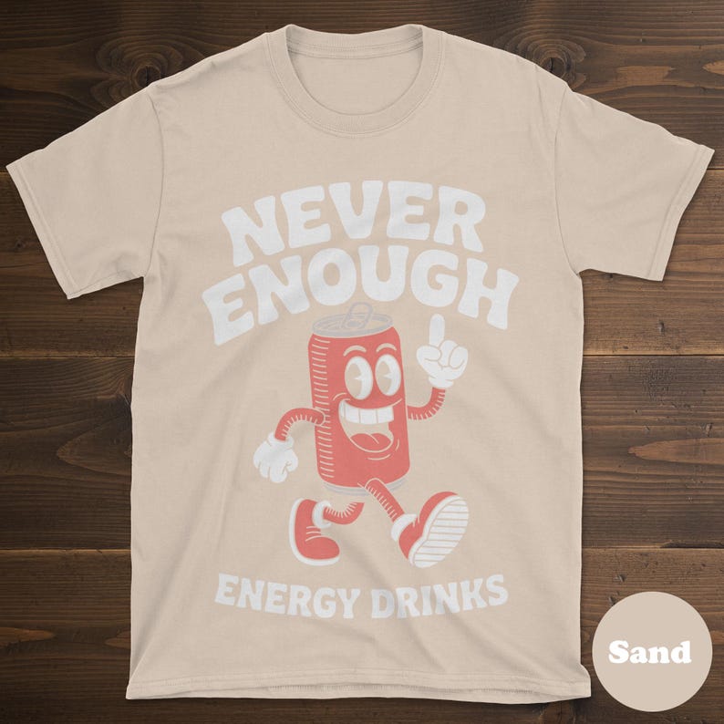 May include: Sand-colored t-shirt with the text "NEVER ENOUGH ENERGY DRINKS" in white. The graphic features a cartoon energy drink can with a smiling face, arms, and legs, pointing upwards. The can is red with white accents.