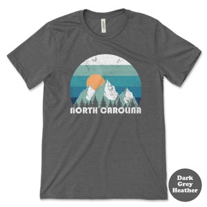 May include: Dark grey heather t-shirt with a vintage-style graphic of mountains, a sunset, and the text "NORTH CAROLINA".
