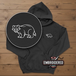 May include: A dark gray hoodie with a white embroidered badger design on the chest and a larger circular design. The hoodie has a front pocket and a hood. The word "EMBROIDERED" is on a label at the bottom.