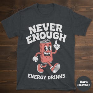 May include: Dark heather gray t-shirt with the words "NEVER ENOUGH ENERGY DRINKS" in white. The shirt features a cartoon image of a smiling energy drink can with arms and legs, pointing upwards.