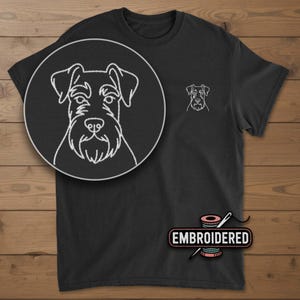 May include: Black t-shirt with a white embroidered Schnauzer dog design. The shirt features a large circular close-up of the dog's face and a smaller version on the chest. The word "EMBROIDERED" is displayed below the shirt.