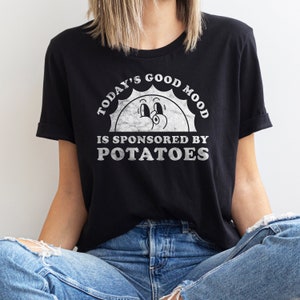 May include: Black t-shirt with a white graphic of a smiling sun with the text "Today's Good Mood Is Sponsored By Potatoes".