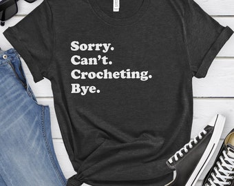 May include: A dark gray t-shirt with the text "Sorry. Can't. Crocheting. Bye." in white.