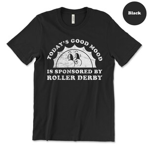 Op de afbeelding: Zwart T-shirt met een witte afbeelding van een lachende zon met de tekst "Today's Good Mood Is Sponsored By Roller Derby".