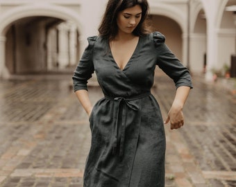 Könnte beinhalten: Eine Frau trägt ein dunkelgrünes Leinen-Wickelkleid mit V-Ausschnitt und einem Bindegürtel. Sie steht in einem Innenhof mit Bogenportalen.