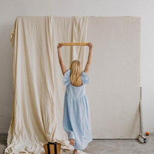 May include: A light blue sleeveless midi dress with ruffled shoulder details and a gathered waistline. The dress features a square neckline and a loose, flowing skirt that falls below the knees, crafted from a solid-colored fabric.