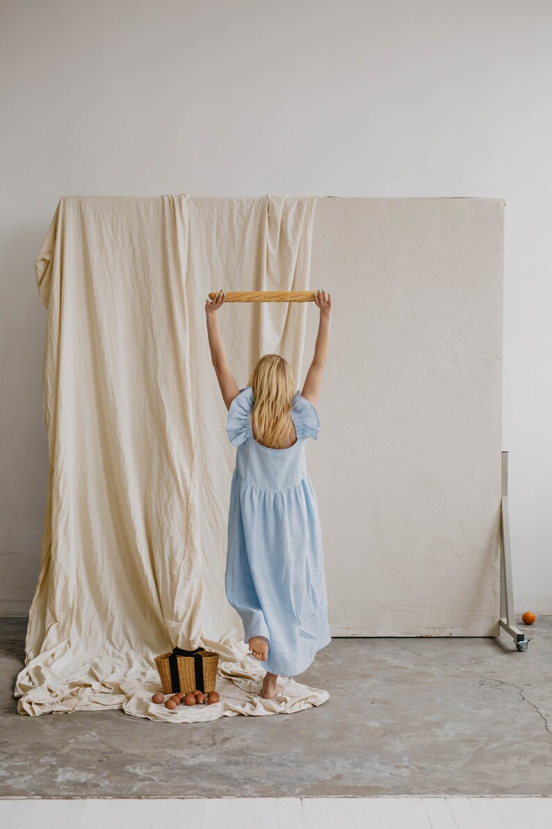 May include: A light blue sleeveless midi dress with ruffled shoulder details and a gathered waistline. The dress features a square neckline and a loose, flowing skirt that falls below the knees, crafted from a solid-colored fabric.