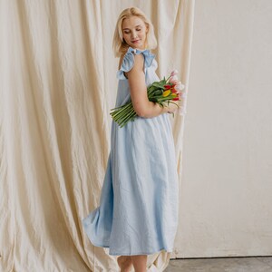 May include: A light blue midi dress featuring ruffled cap sleeves and a loose, flowing silhouette. The garment is crafted from a solid-colored fabric and is paired with a bouquet of fresh tulips in shades of pink, yellow, and white.