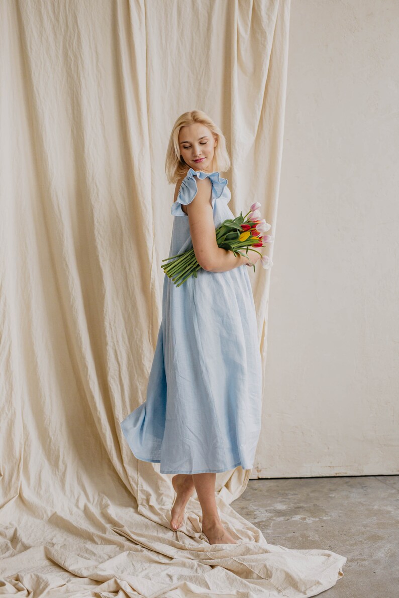 May include: A light blue midi dress featuring ruffled cap sleeves and a loose, flowing silhouette. The garment is crafted from a solid-colored fabric and is paired with a bouquet of fresh tulips in shades of pink, yellow, and white.