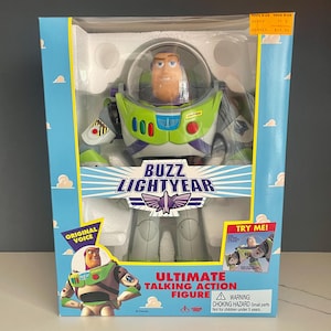 May include: A Buzz Lightyear action figure in a box. The figure is wearing a white and green spacesuit with a purple chest piece. The box has a picture of Buzz Lightyear on the front and says "Ultimate Talking Action Figure" and "Try Me!" on the box.