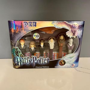 May include: A box of Harry Potter collectible PEZ dispensers. The box features a colorful image of Hogwarts castle and a group of characters from the Harry Potter series. The dispensers are in the shape of Harry Potter, Ron Weasley, Hermione Granger, Draco Malfoy, and Severus Snape. The box is labeled "Harry Potter Limited Edition".