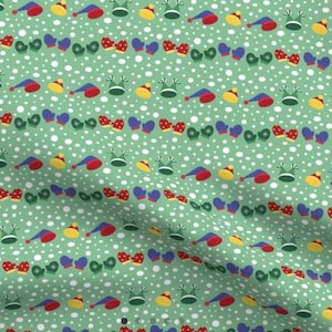 May include: A green fabric with a repeating pattern of red, blue, yellow, and green hats and mittens. The background is white with small white dots.