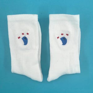 Könnte beinhalten: Ein Paar weiße Socken mit einem blauen Bowlingball und roten Pins, die auf jeder Socke gestickt sind.