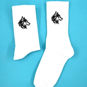 Könnte beinhalten: Ein Paar weiße Socken mit einem gestickten schwarzen Wolfskopfdesign auf jeder Socke.