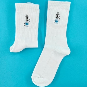Könnte beinhalten: Ein Paar weiße Socken mit einem gestickten Cartoon-Shisha-Design in Schwarz, Grau und Blau. Die Socken sind aus einem weichen, gerippten Material. Der Hintergrund ist ein leuchtendes Blau. Ein lustiges Accessoire.