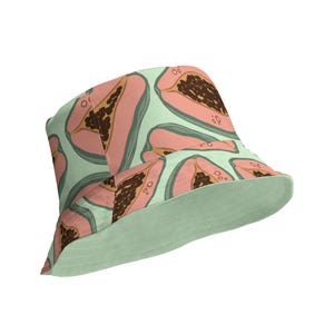 Può includere: Un cappello a secchiello verde con stampa di papaya. Il cappello ha un'ampia tesa ed è realizzato in un tessuto leggero.