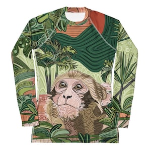 Puede incluir: Una camisa de manga larga con estampado de jungla verde, marrón y naranja. La camisa presenta una ilustración detallada de la cara de un mono en el centro.