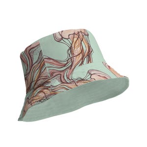 Può includere: Un cappello a secchiello verde chiaro con un motivo astratto di meduse marroni e arancioni.