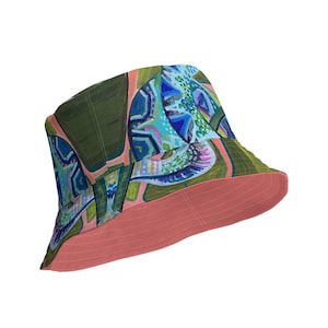 Può includere: Un cappello a secchiello verde e rosa con un motivo astratto colorato. Il cappello ha un'ampia tesa e una corona piatta.