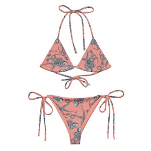 Puede incluir: Un bikini de color rosa coral con una parte superior triangular y una parte inferior con cordones laterales. El bikini está estampado con un patrón de pulpos grises.
