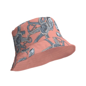 Può includere: Un cappello a secchiello rosa con una stampa di polpo blu e bianco. Il cappello ha un'ampia tesa e una corona piatta.