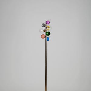 Puede incluir: Una lámpara de pie moderna con acabado de latón y una serie de pantallas de globo de cristal de colores. Las pantallas son de varios colores, incluyendo rosa, azul, verde y morado. La lámpara tiene una base redonda.
