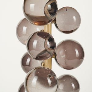 May include: A modern lamp featuring a cluster of smoky gray glass globes attached to a brass-colored metal frame. The lamp has a gold-colored, rectangular top. The glass globes are arranged in a cascading pattern.