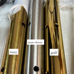May include: Close-up of three cylindrical metal lamp parts in honey, matte chrome, and gold finishes. Each part has a series of small holes. The honey and gold parts have a shiny finish, while the matte chrome is a muted silver color.