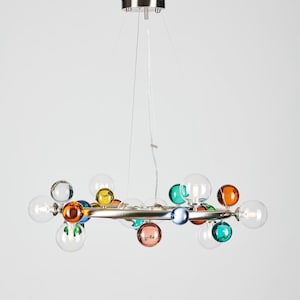 May include: A modern chandelier with a silver metal frame and multiple clear glass bulbs. The bulbs are interspersed with colorful glass spheres in shades of orange, green, blue, pink, and yellow. The fixture hangs from a silver ceiling mount.