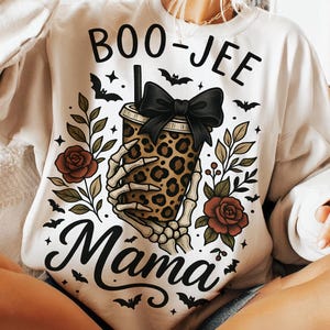 Op de afbeelding: Cr&egrave;mekleurige sweatshirt met een Halloween-thema. Het ontwerp toont een beker met luipaardprint die wordt vastgehouden door een skelet, een zwarte strik, rozen, vleermuizen en de woorden "BOO-JEE Mama".