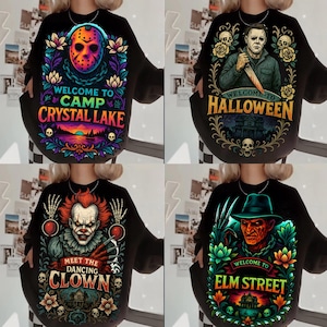 May include: Four black sweatshirts featuring horror movie graphics. Top left: Jason mask with "Welcome to Camp Crystal Lake". Top right: Michael Myers with "Welcome to Halloween". Bottom left: Pennywise with "Meet the Dancing Clown". Bottom right: Freddy Krueger with "Welcome to Elm Street".