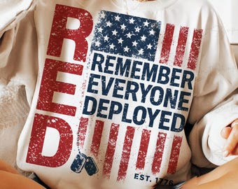 Peut inclure: Sweat-shirt crème avec un motif de drapeau américain vieilli. Le drapeau présente des rayures rouges et un champ d'étoiles bleu, avec les mots "RED" et "REMEMBER EVERYONE DEPLOYED" en rouge et bleu. Comprend le texte "EST. 1776".