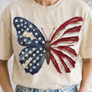 May include: A beige t-shirt featuring a large butterfly design. The butterfly's wings are crafted to resemble the American flag, with blue denim wings adorned with white stars and red and white striped wings.