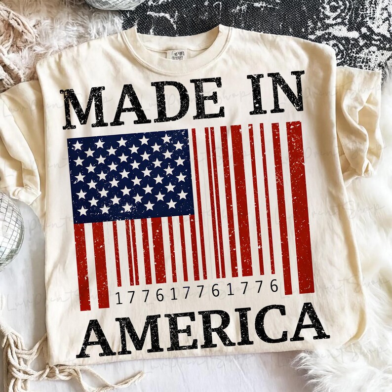 Peut inclure: T-shirt cr&egrave;me avec un motif vieilli du drapeau am&eacute;ricain en forme de code-barres. Les mots "MADE IN AMERICA" sont imprim&eacute;s en noir, avec le code-barres affichant les chiffres "177617761776".
